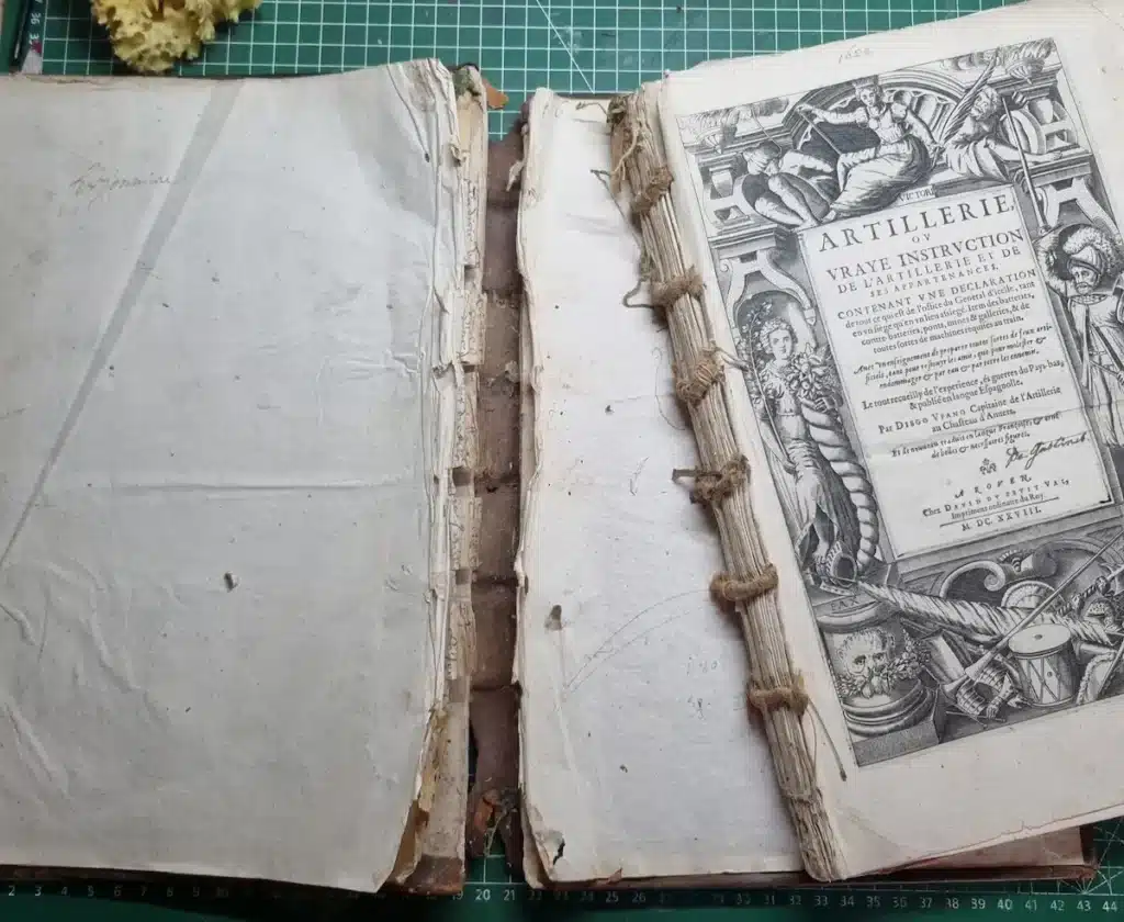 Dos d'un livre ancien sans couvrure, ficelles de couture transversales reliant les cahiers, page de titre Artillerie 1628